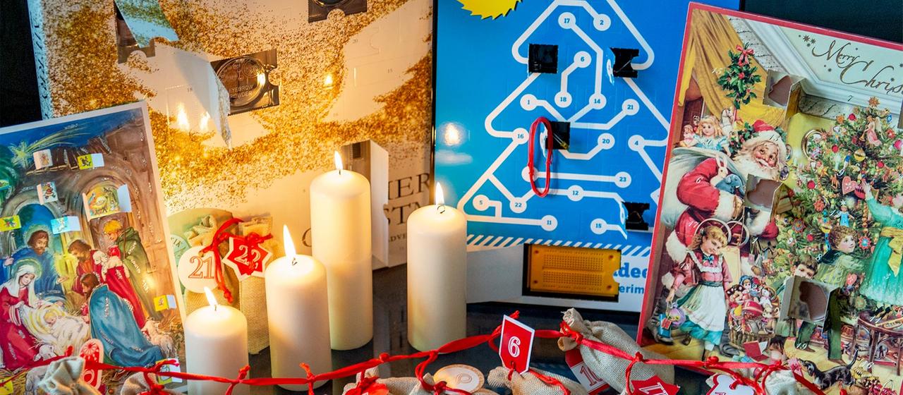 Verschiedene Adventskalender und vier brennende Kerzen.