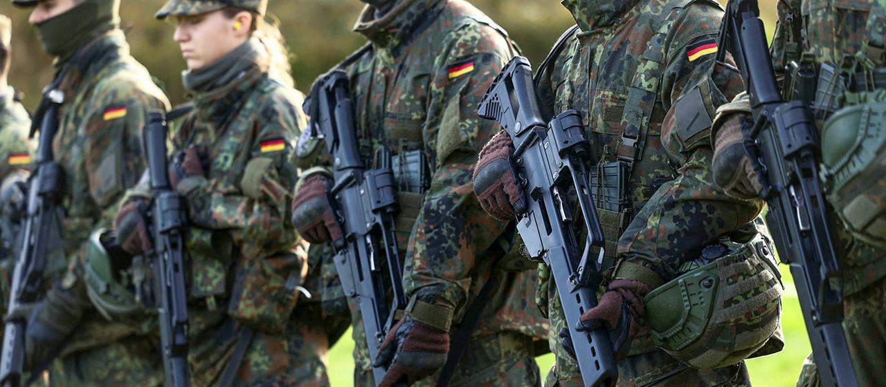 Rekruten der Bundeswehr stehen in einer Reihe und halten Gewehre.
