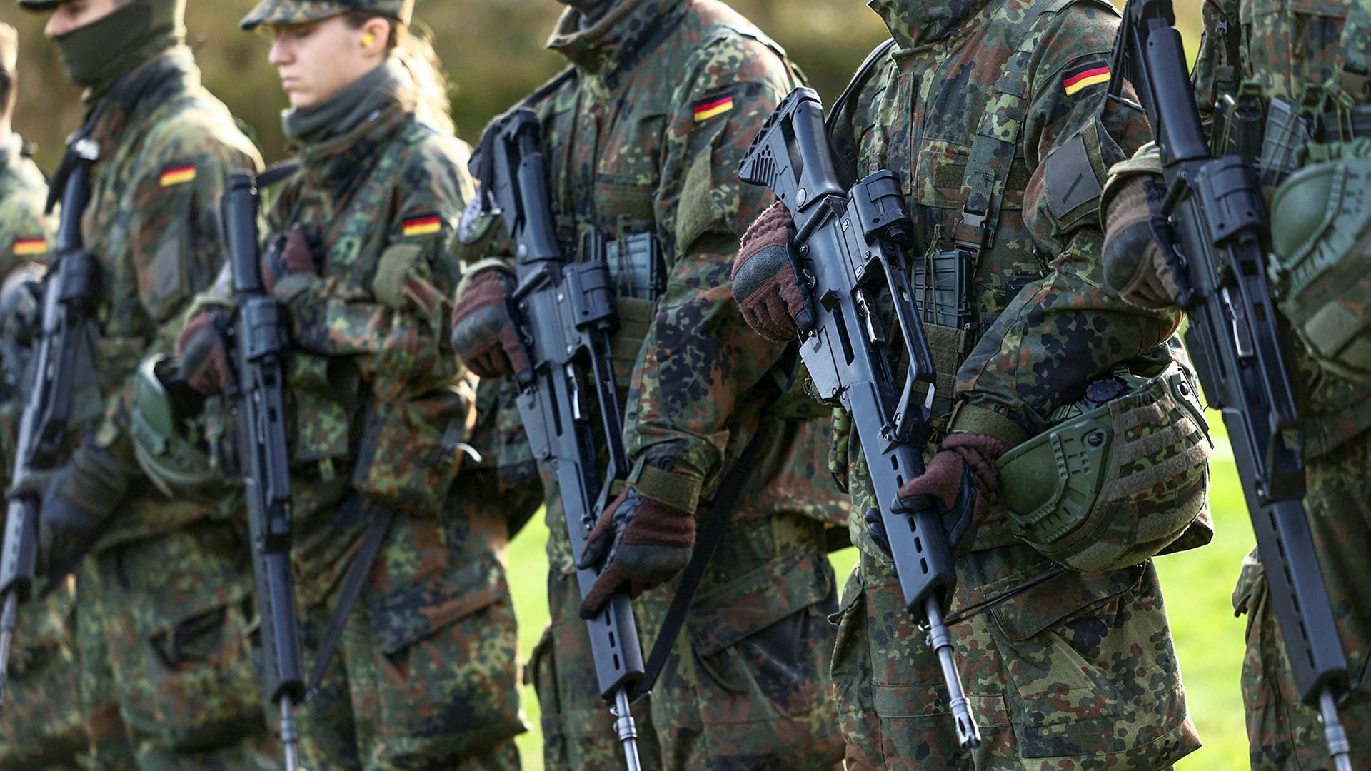 Rekruten der Bundeswehr stehen in einer Reihe und halten Gewehre. | REUTERS