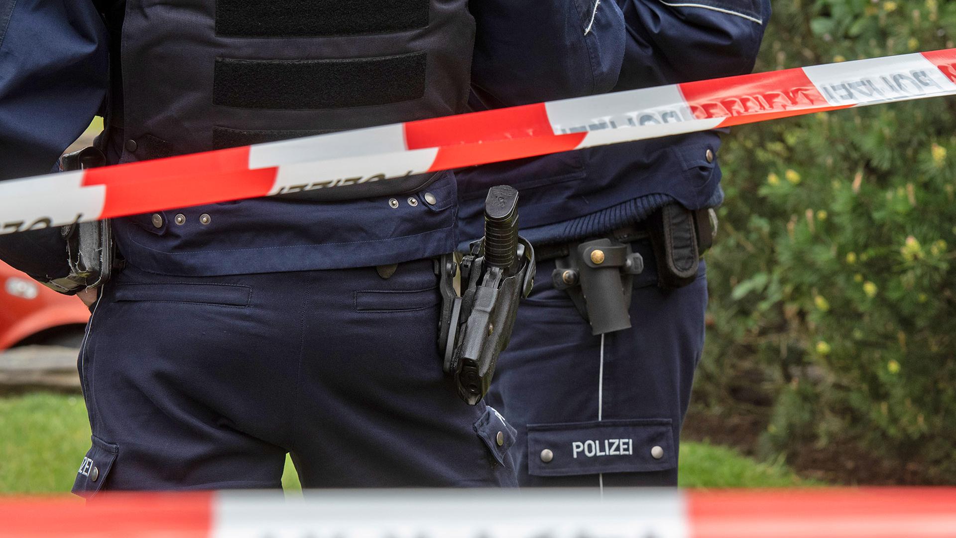 Symbolbild: Polizisten stehen am Tatort hinter einem Absperrband (Quelle: picture alliance/dpa/B.Thissen) | picture alliance/dpa/B.Thissen