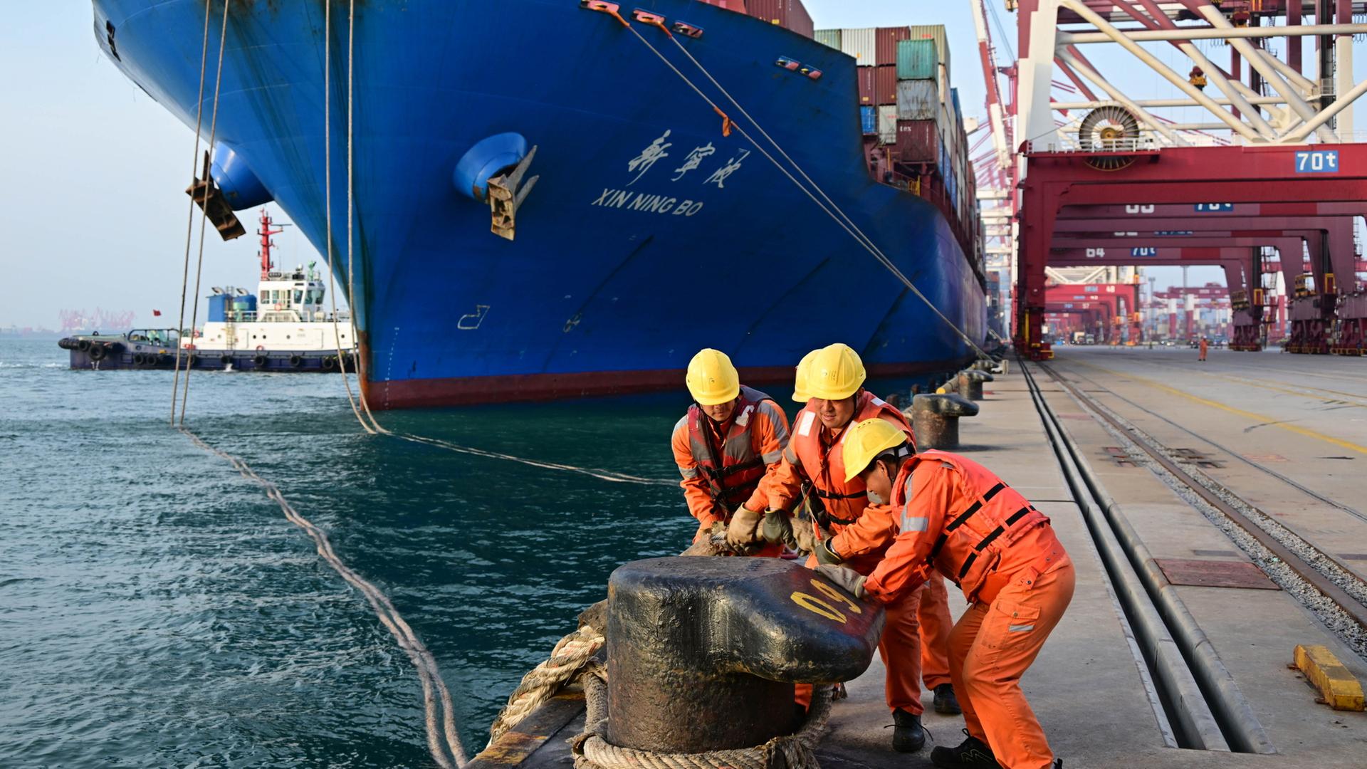 Arbeiter machen in einem Containerdock des Hafens von Qingdao die Leinen für ein Schiff los.