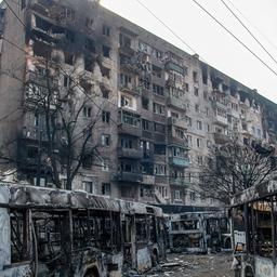Vor einem durch Bomben zerstörten Hochhaus stehen ausgebrannte Linienbusse.
