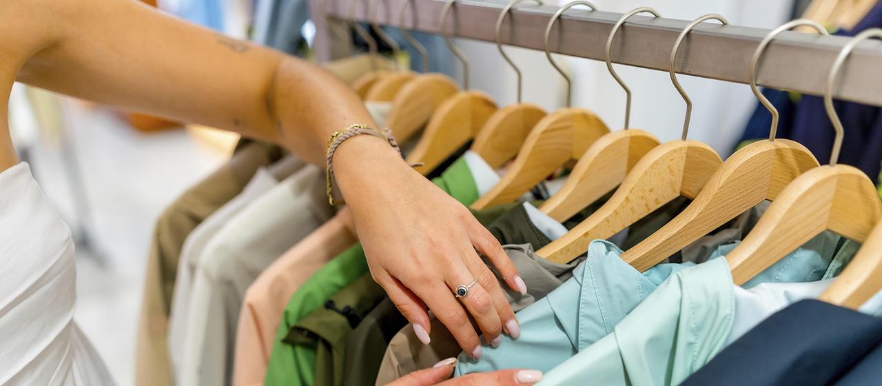 Una mujer busca chaquetas colgadas en perchas en una tienda.