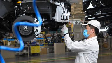 Ein Mann arbeitet mit Mund-Nasen-Schutz an einem Auto im Autowerk Xinjiang von GAC Motor in Urumqi (China).