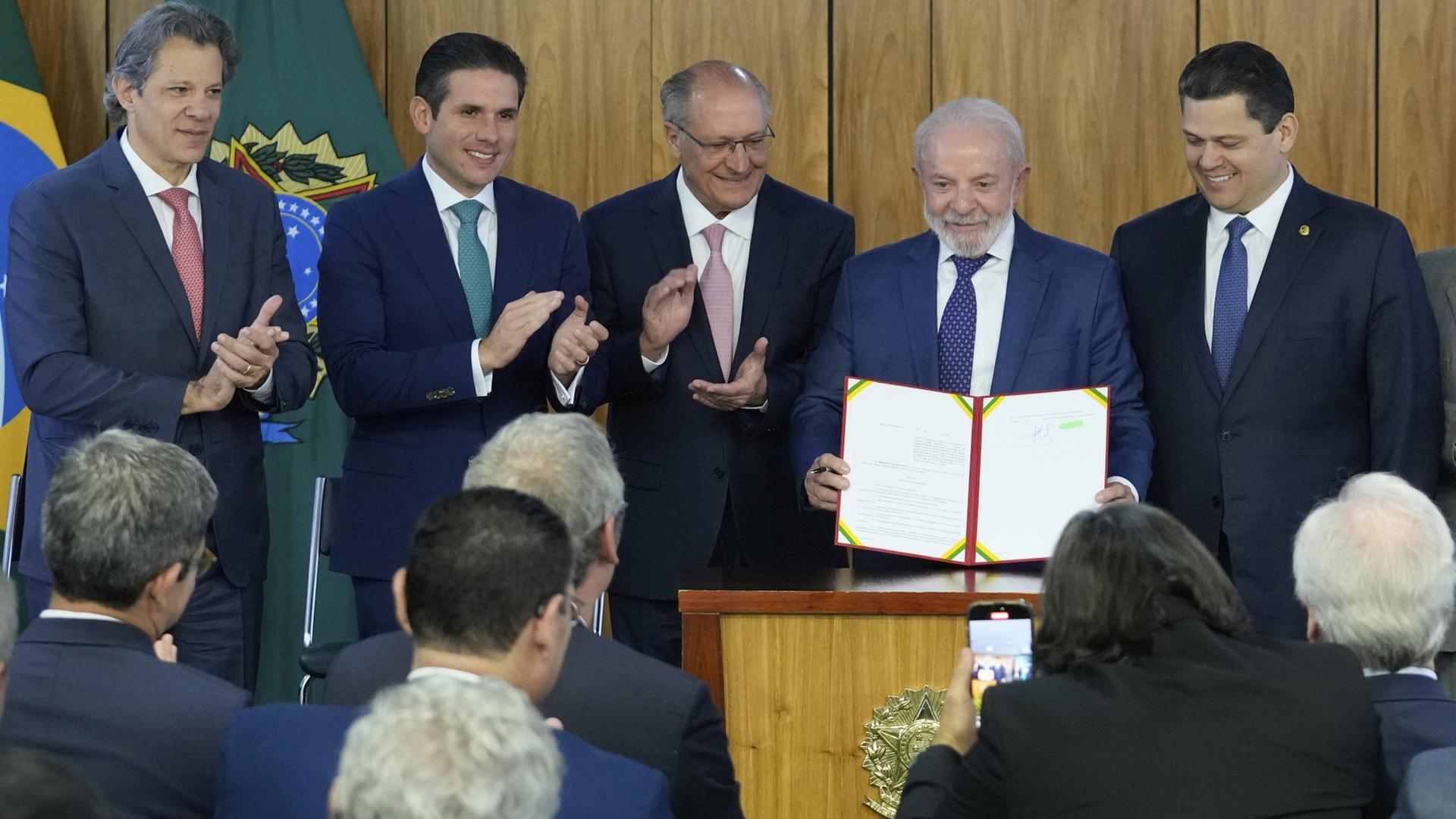 Brasiliens Präsident Lula präsentiert umringt von Politikern eine Urkunde. | dpa