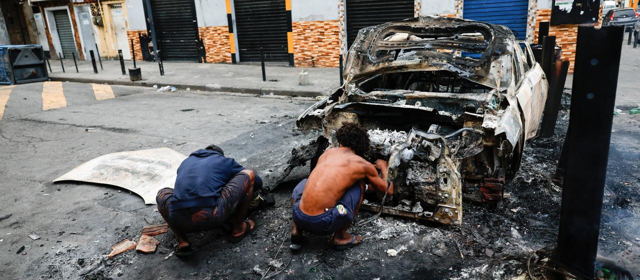 Menschen ducken sich hinter einem ausgebrannten Polizeiauto in Rio de Janeiro.
