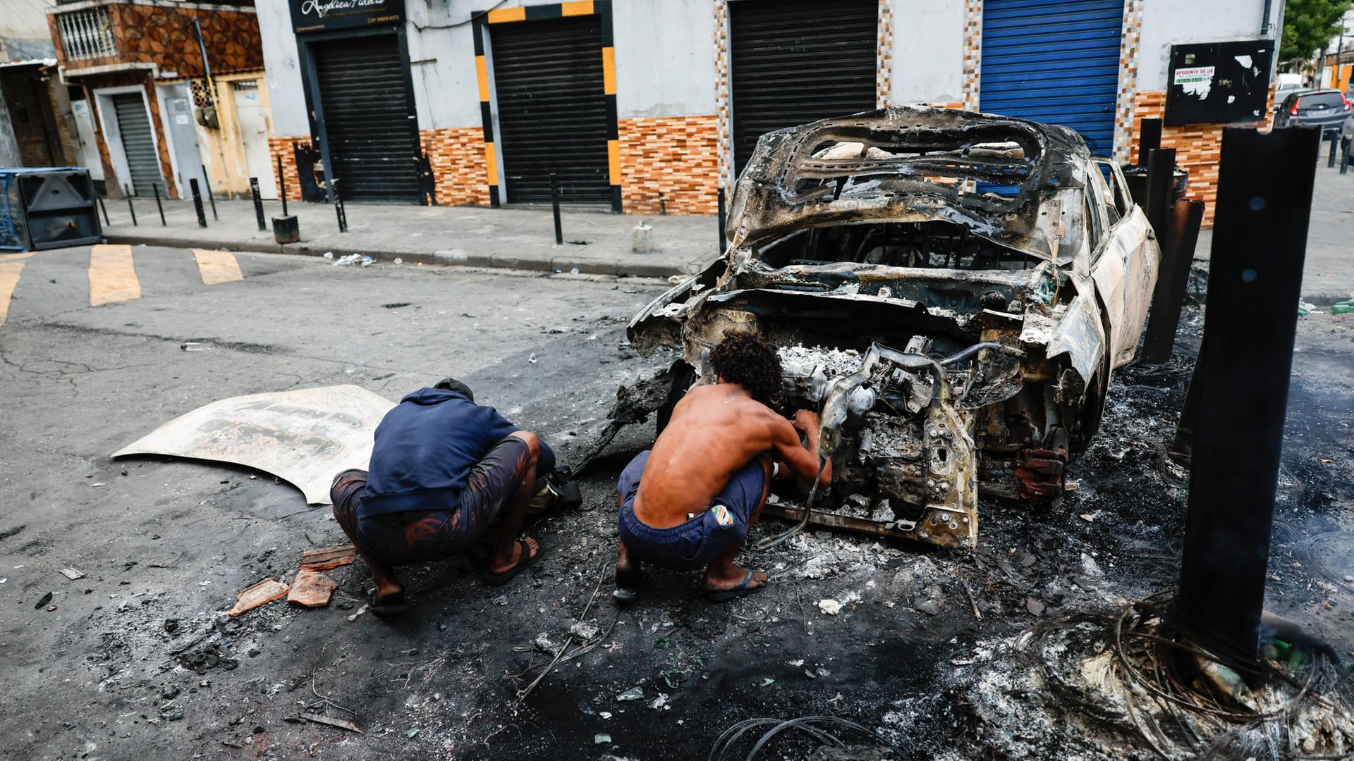 Menschen ducken sich hinter einem ausgebrannten Polizeiauto in Rio de Janeiro. | EPA