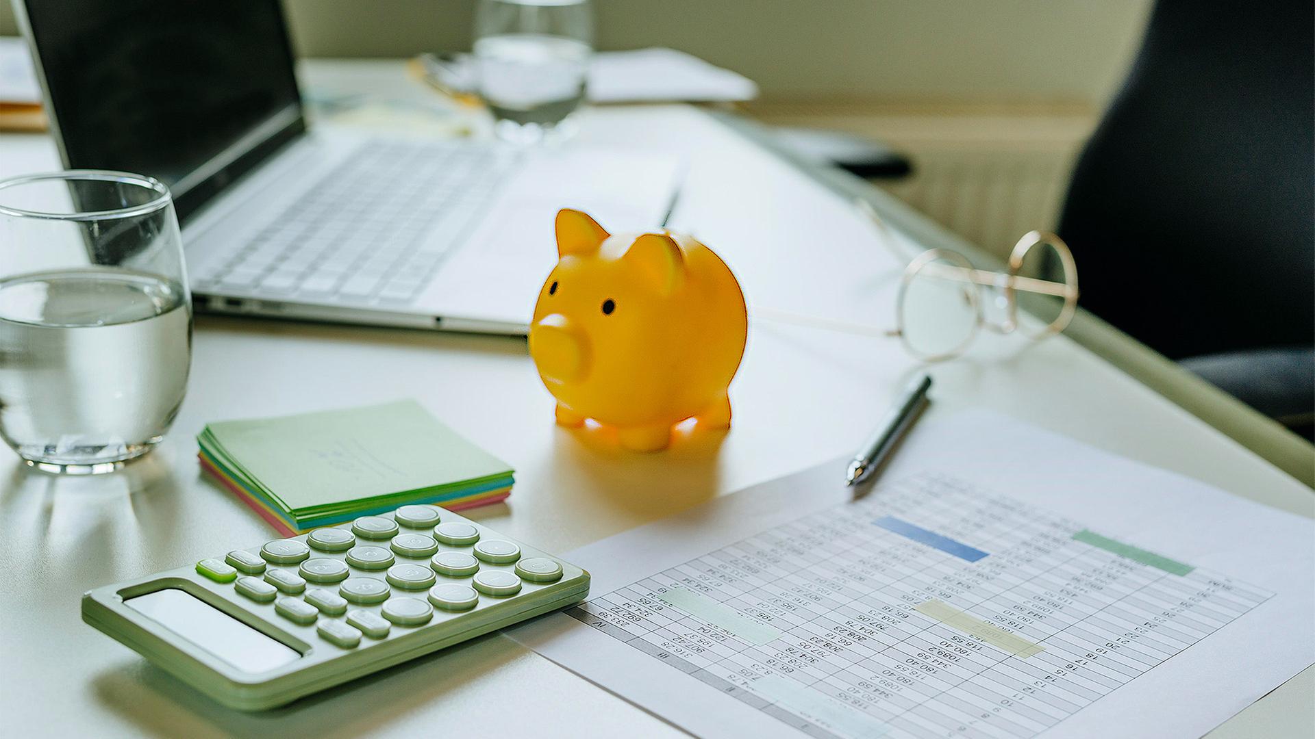 Sparschwein, Taschenrechner, Kalkulationstabelle und ein Laptop auf einem Tisch. | picture alliance / Westend61