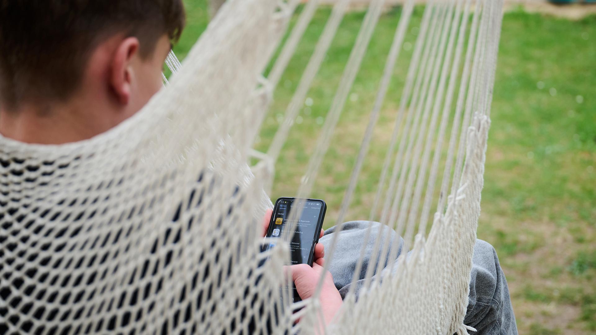 Ein Jugendlicher sitzt mit Smartphone in der Hängematte. | dpa