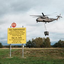 Ein Bundeswehr-Hubschrauber hebt mit angehängter Last ab. Im Vordergrund steht ein Schild, das vor dem Flugbetrieb warnt.