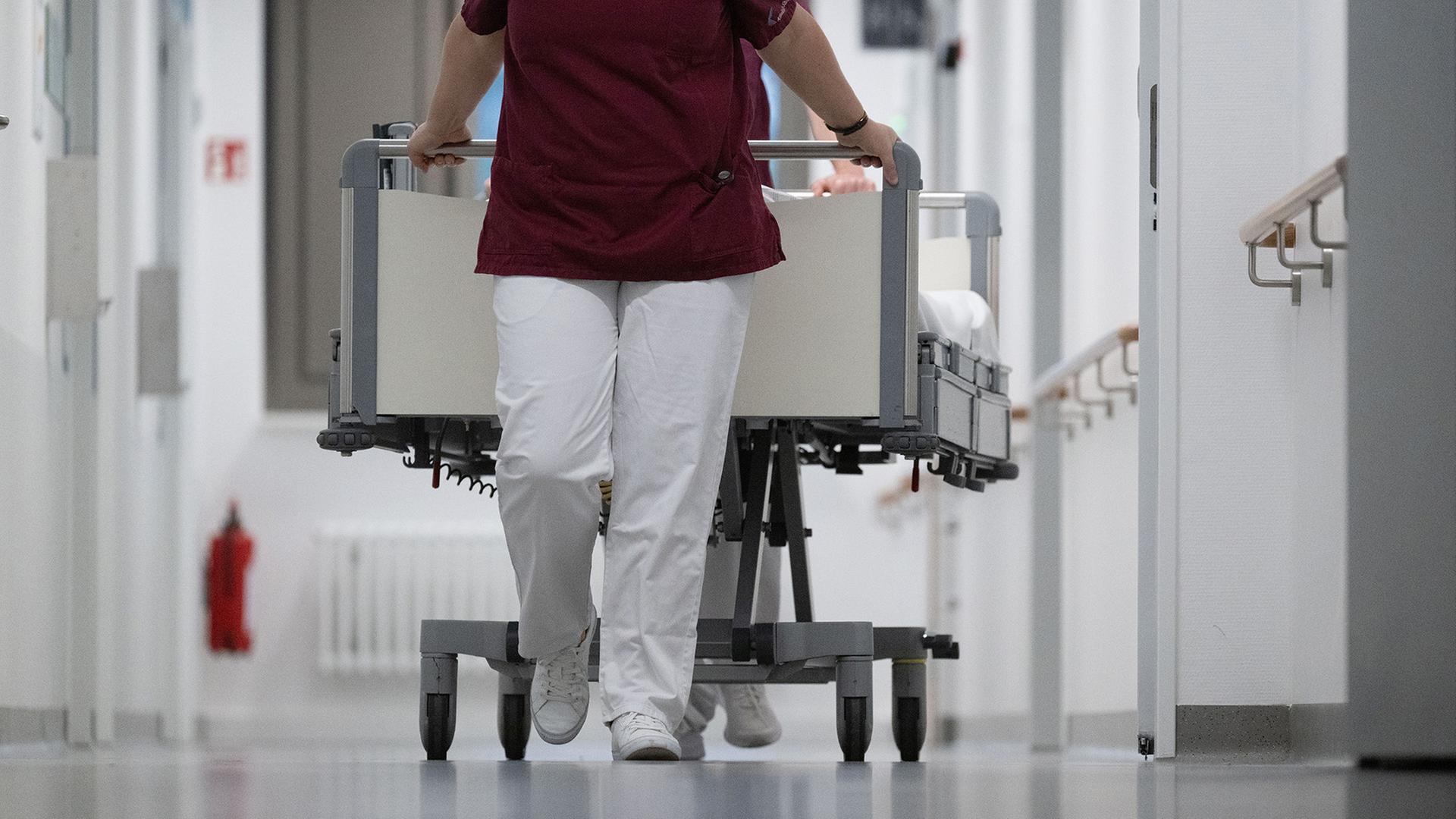 Eine Krankenpflegerin und ein Krankenpfleger schieben ein Krankenbett durch den Gang einer Station eines Krankenhauses. | dpa