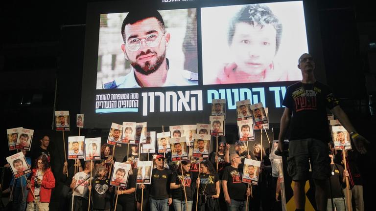 Menschen halten in Tel Aviv Fotos von noch zwei im Gazastreifen festgehaltenen toten Geiseln hoch.