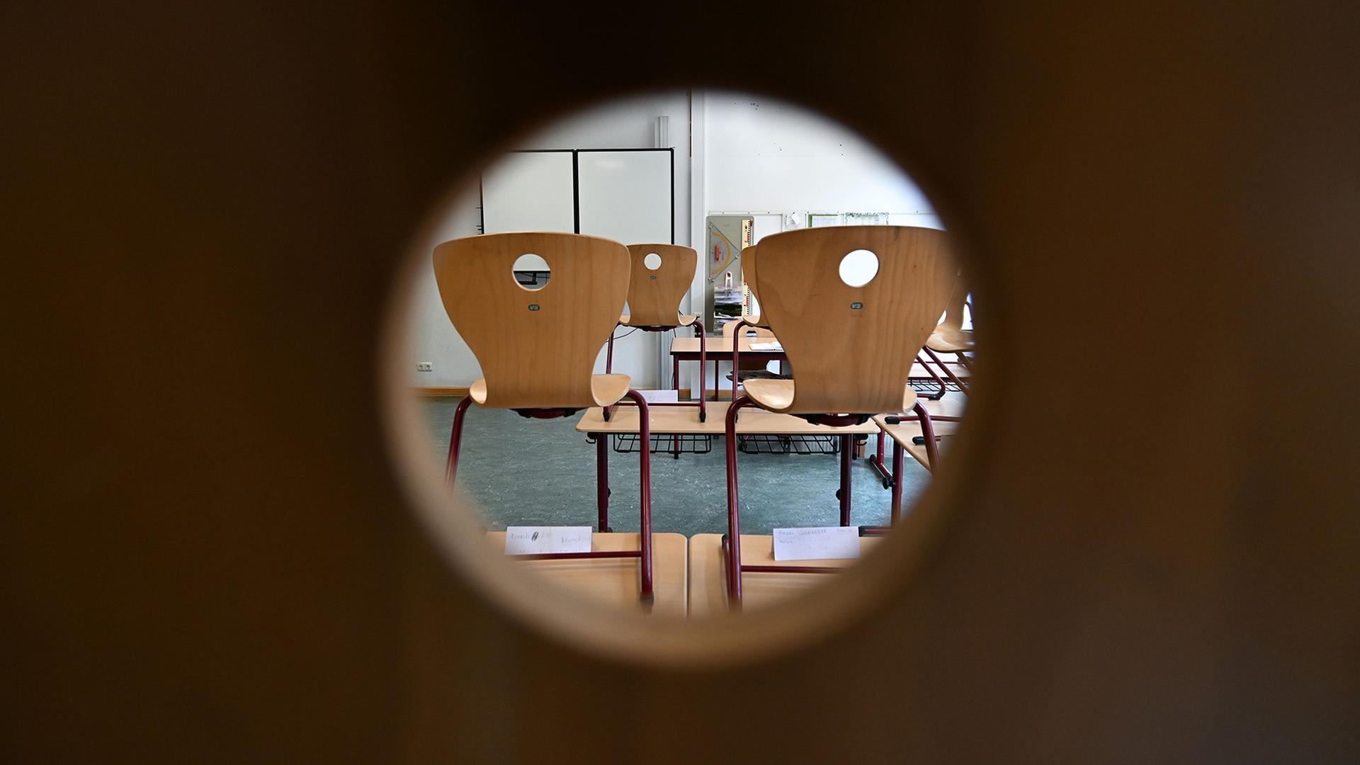 Durch ein Loch einer Stuhllehne, sieht man einen leeren Klassenraum. | Arne Dedert/dpa