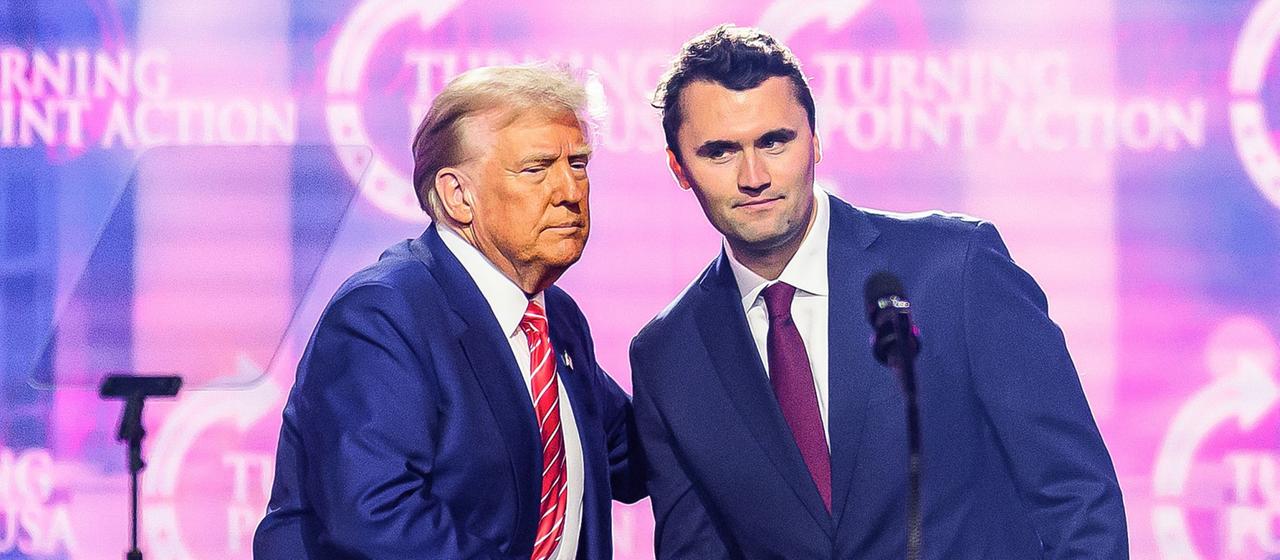 Donald Trump und Charlie Kirk geben sich auf einer Bühne die Hand. (Archivbild: 22.12.2024)