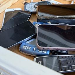 Mehrere Smartphones und ältere Handy-Modelle liegen in einer Holzschublade.