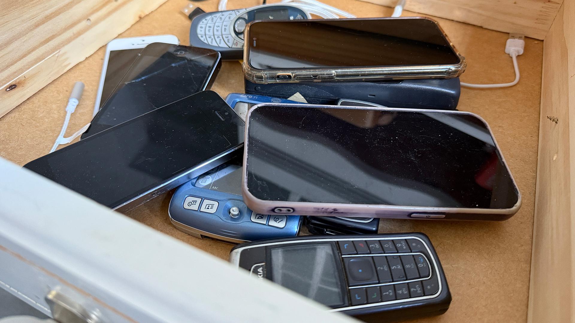 Mehrere Smartphones und ältere Handy-Modelle liegen in einer Holzschublade. | Jens Eberl / WDR