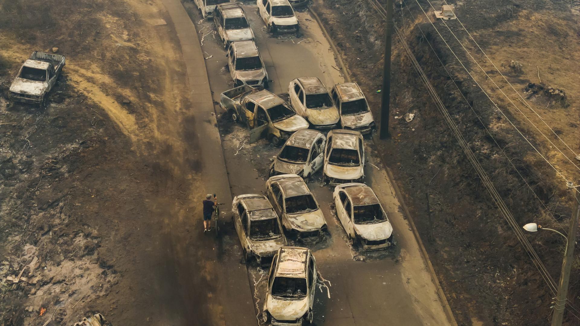 In der Stadt Lirquen in Chile stehen beschädigte Fahrzeuge an einer Straße, nachdem Waldbrände durch Wohngebiete gezogen waren | dpa