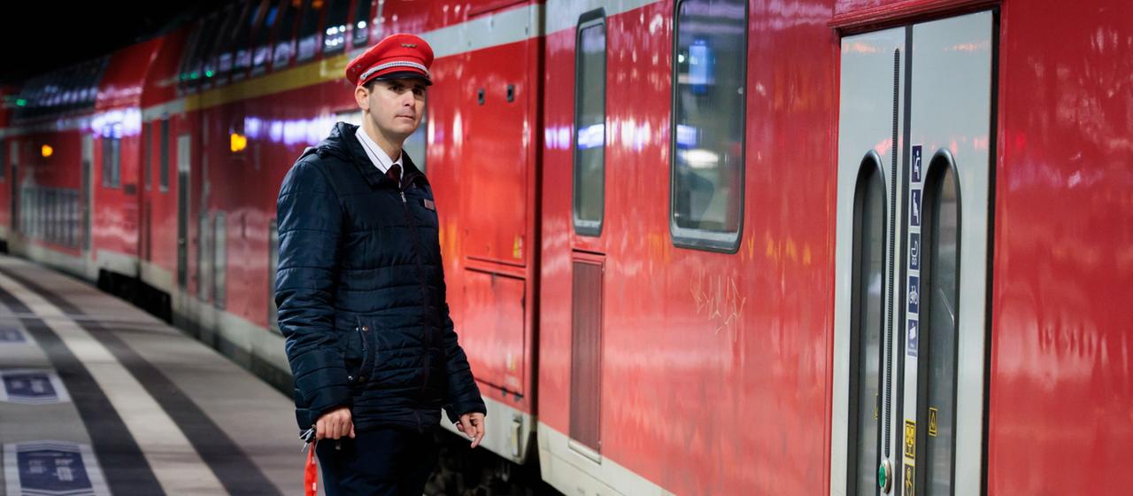 Ein Schaffner steht vor einem Zug.