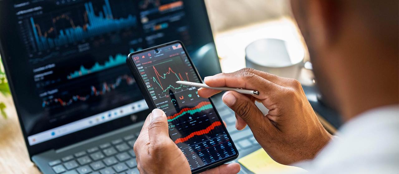 Eine Person überprüft Börsenkurse auf einem Smartphone- und Laptop-Bildschirm.