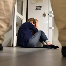 Gestelltes Bild: Eine Person steht vor einer Frau, die sich schützend in eine Zimmerecke drückt.