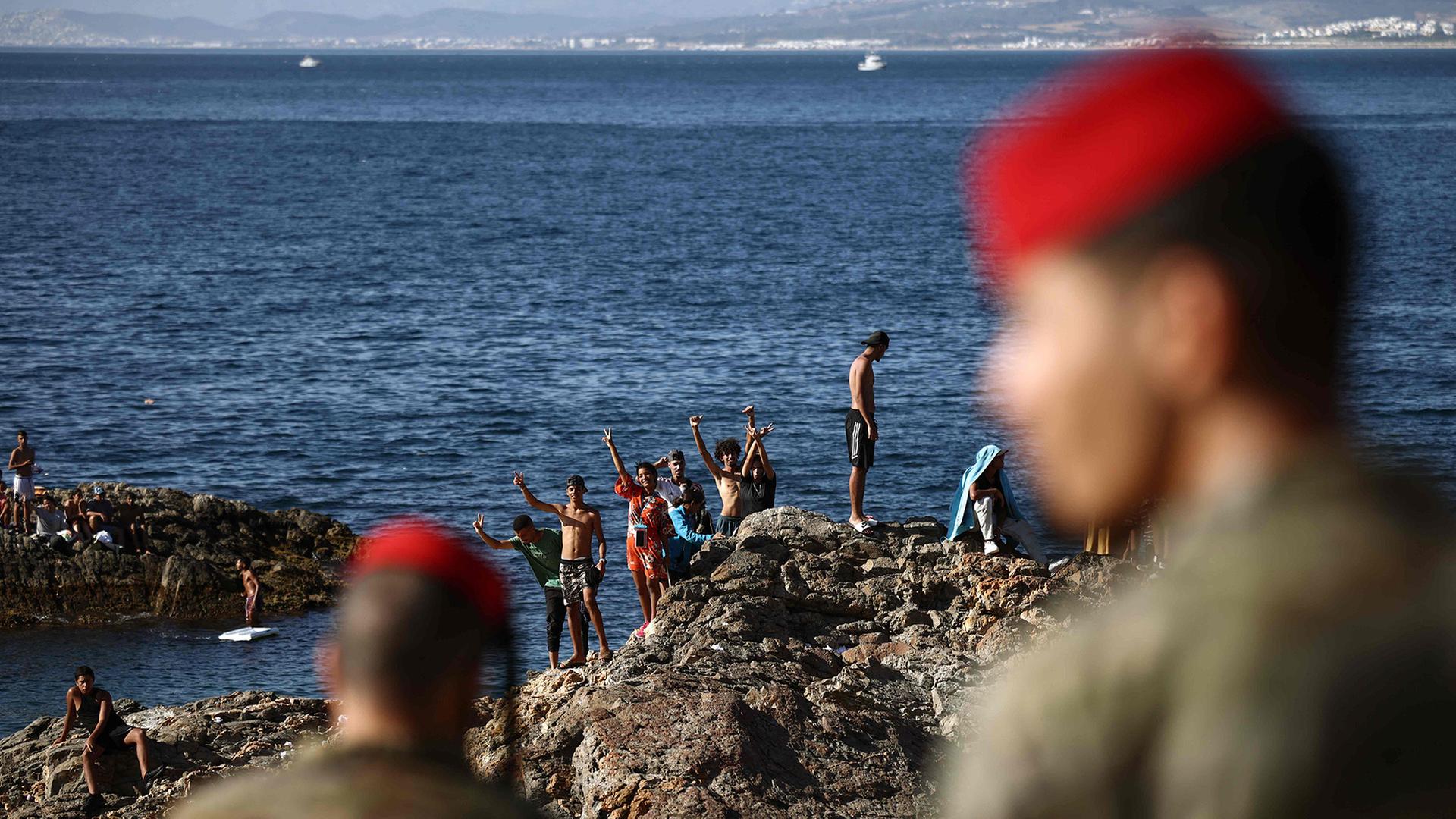 Angehörige der spanischen Armee beobachten eine Gruppe von Migranten nahe dem Grenzübergang der spanischen Exklave Ceuta. | AFP