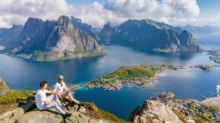 Zwei Wanderer entspannen sich auf einem Felsvorsprung und bewundern den atemberaubenden Panoramablick auf die Lofoten.