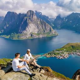 Zwei Wanderer entspannen sich auf einem Felsvorsprung und bewundern den atemberaubenden Panoramablick auf die Lofoten.