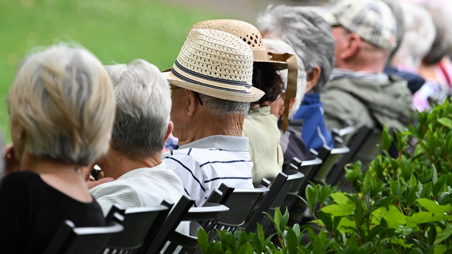 Mehrere ältere Personen sitzen nebeneinander auf Stühlen im Freien. | dpa