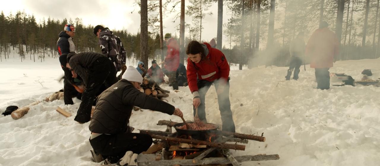 Junge Menschen bereiten auf einem Lagerfeuer Essen bei einer Übung im Freien zu.