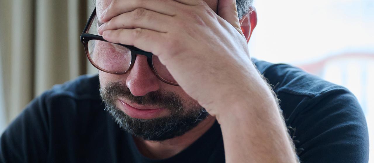 Ein Mann hält sich den Kopf und seufzt.
