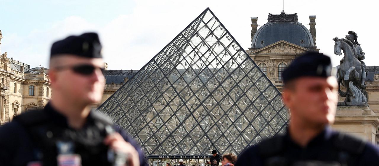 Zwei Polizisten stehen vor der Pyramide des Pariser Louvre.