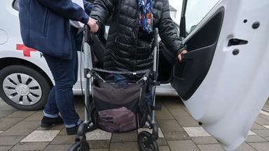 Eine Pflegefachperson hilft einer Person mit Rollator aus dem Auto