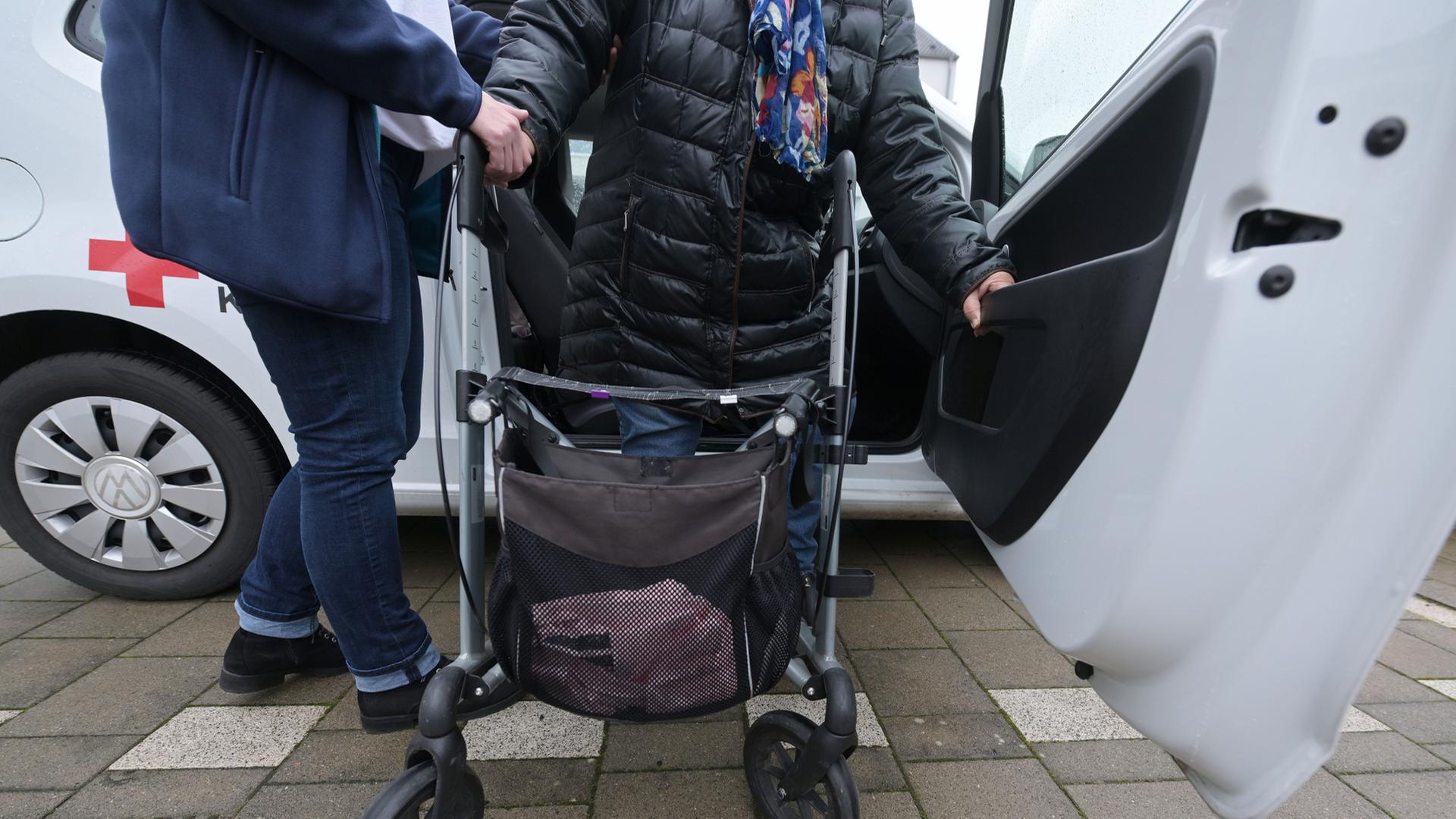 Eine Pflegefachperson hilft einer Person mit Rollator aus dem Auto | dpa