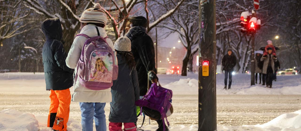 Eine Mutter trägt die Schulranzen ihrer Kinder während sie im Schnee an einer Fußgängerampel in Hamburg warten.