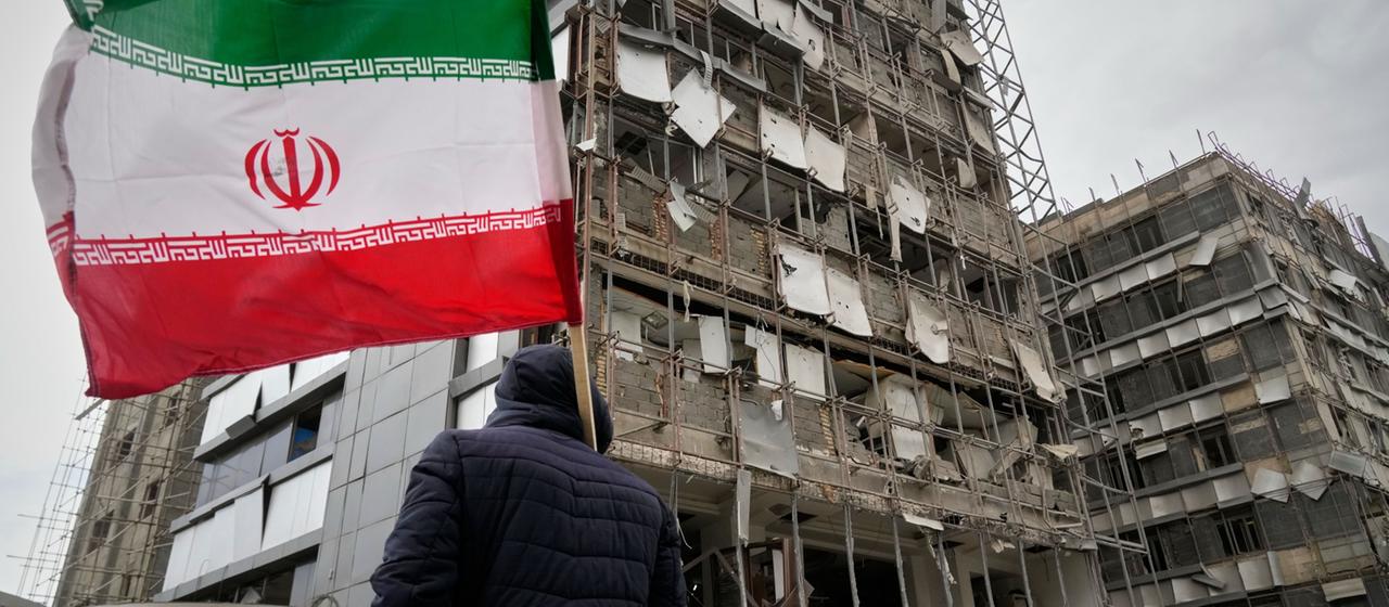 Ein Mann hält eine iranische Fahne neben einem durch Angriffe beschädigten Krankenhaus in Teheran. 