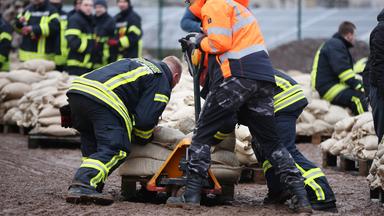 Helfer beladen im Schlamm eine Hubwagen mit Sandsäcken.