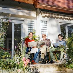 Eine Familie sitzt vor einem Haus auf einer Terrasse.
