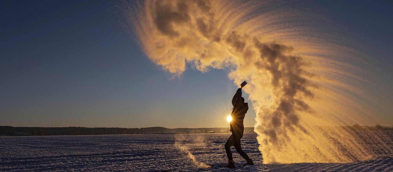 Frau wirft heißes Wasser in die Luft, das zu Eiskristallen gefriert.