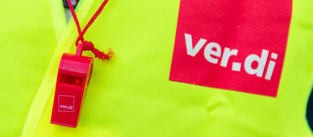 eine gelbe Warnweste mit dem Ver.di-Schriftzug und einer roten Trillerpfeife
