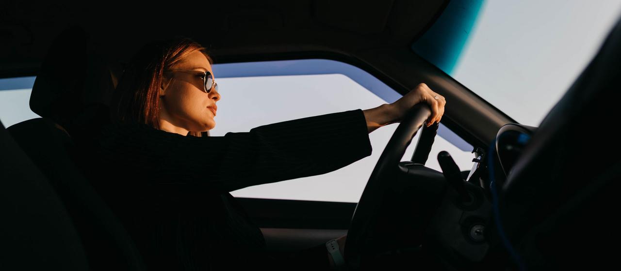  Eine junge Frau mit Sonnenbrille beim Autofahren.