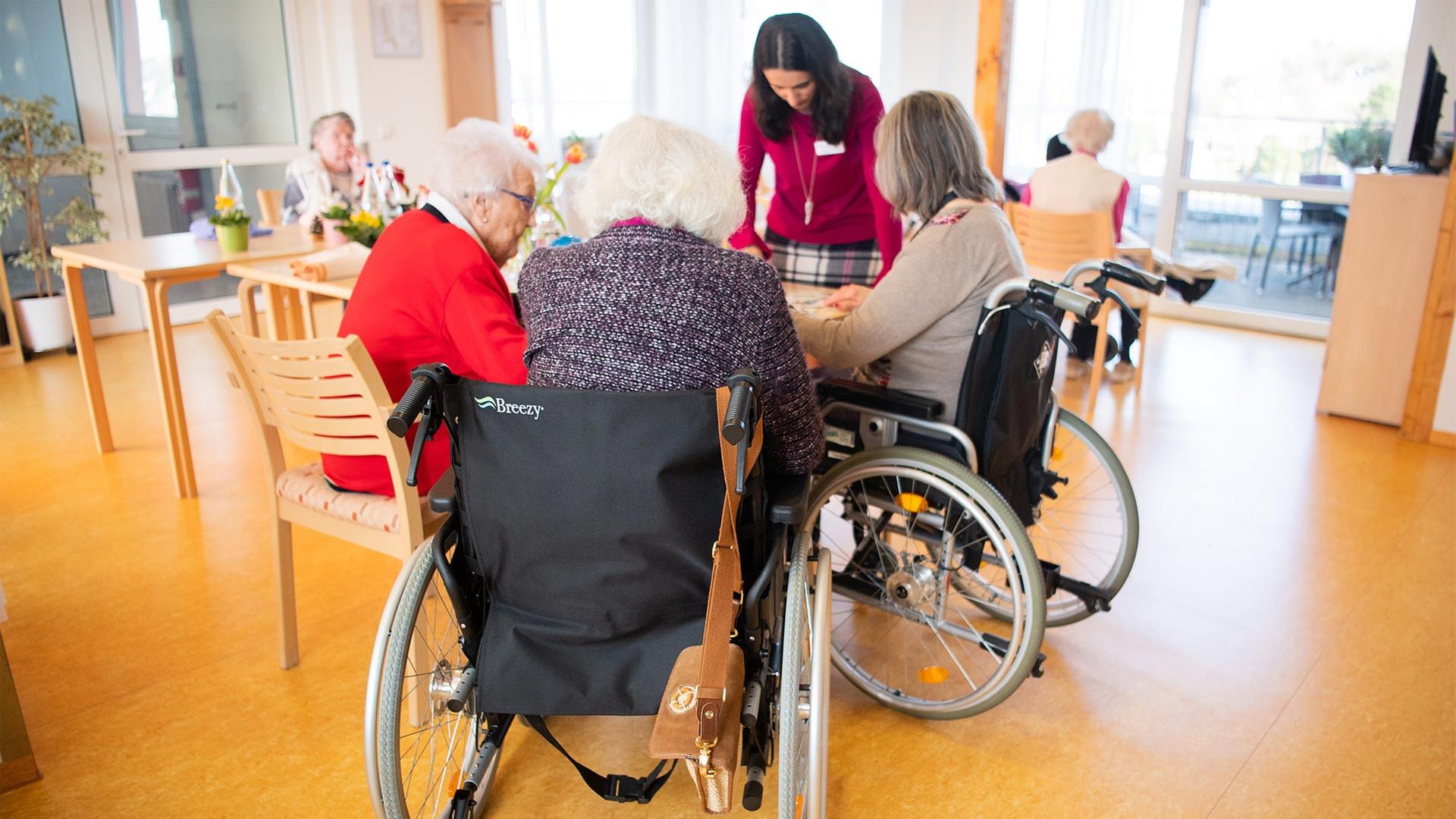 Bewohnerinnen eines Pflegeheims sitzen in Rollstühlen um einen Tisch.