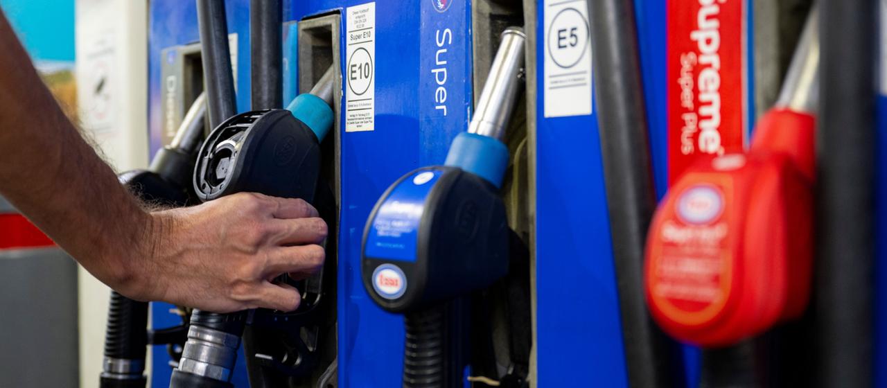 Ein Autofahrer hängt an einer Tankstelle eine Zapfpistole in die Zapfsäule.