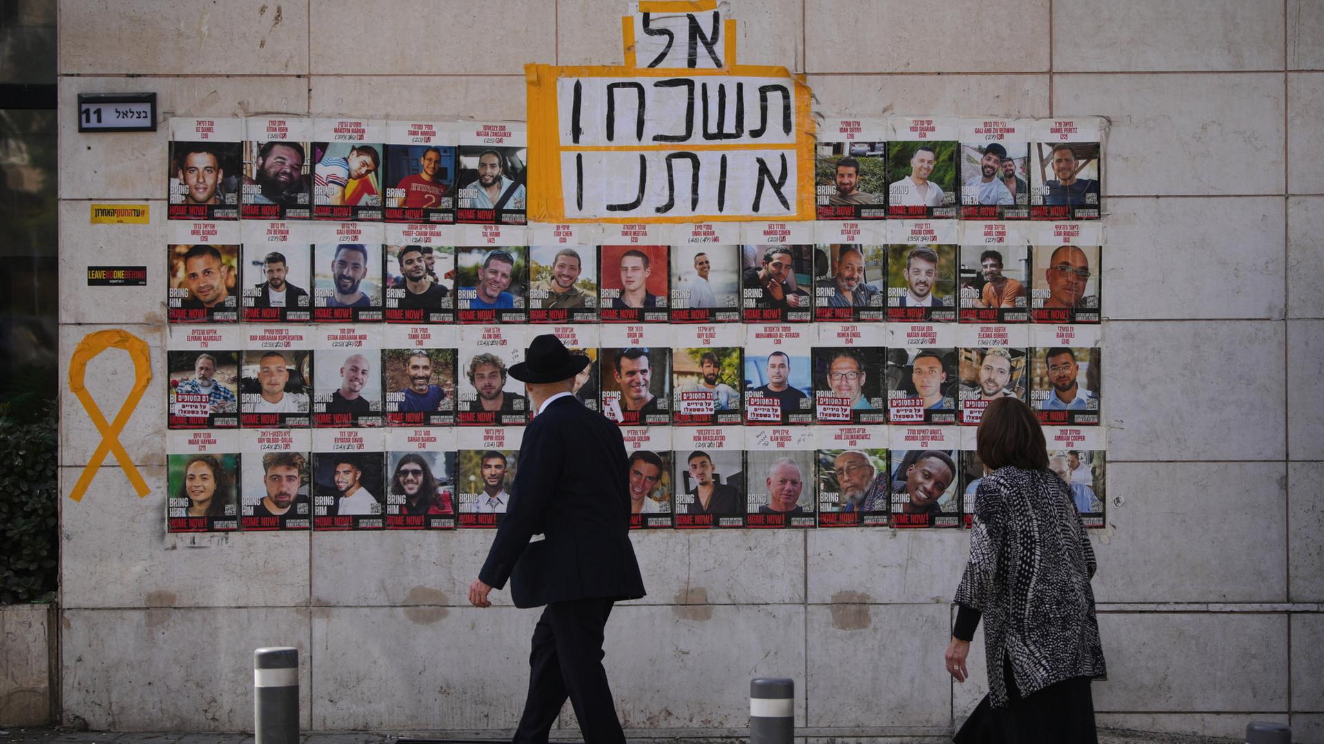 Menschen gehen in Jerusalem an einer Wand vorbei, an der Fotos von Geiseln aufgehängt sind. | AP