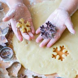 Ausgerollter Plätzchen Teig auf einer Arbeitsfläche mit den Händen von einem Kind mit einer weihnachtlichen Ausstechform.