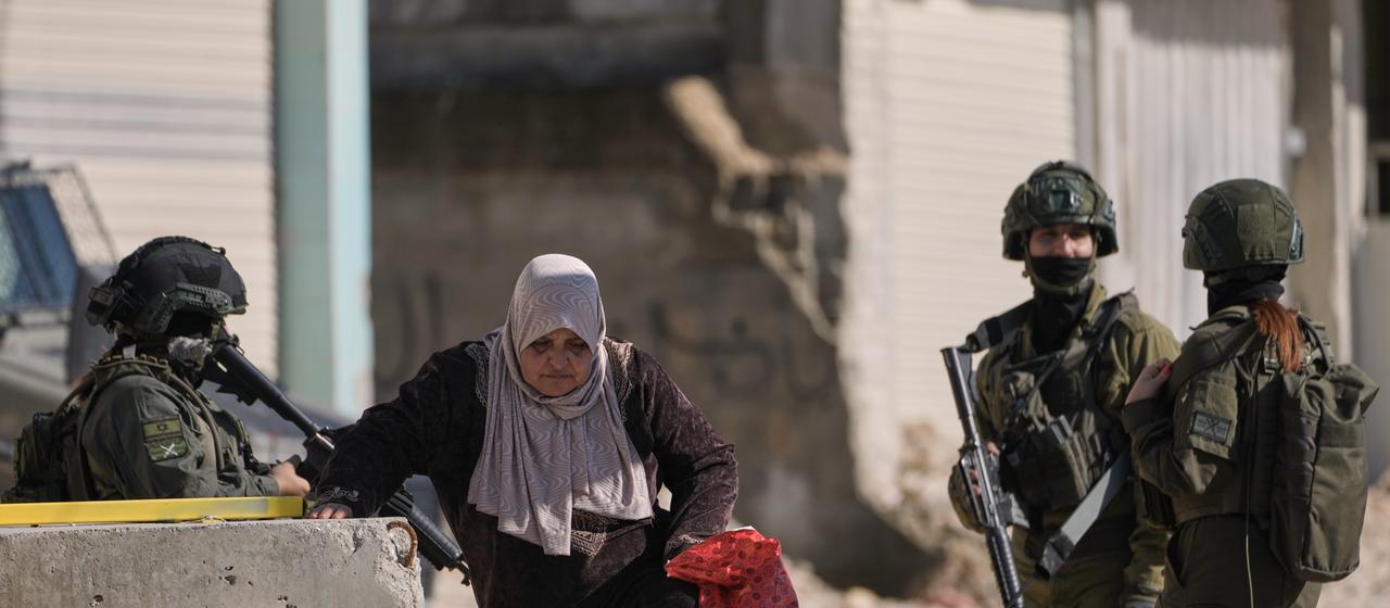   Tulkarem: A Palestinian woman walks past Israeli soldiers