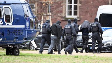 Zwei Personen werden von Polizisten bei einem Hubschrauberlandeplatz in Karlsruhe von einem Hubschrauber zu einem Auto geführt. 