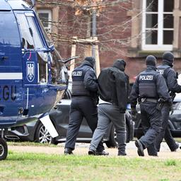Zwei Personen werden von Polizisten bei einem Hubschrauberlandeplatz in Karlsruhe von einem Hubschrauber zu einem Auto geführt. 