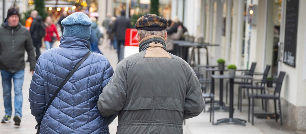 Ein älteres Paar geht Arm in Arm durch eine Einkaufsstraße in Schwerin.