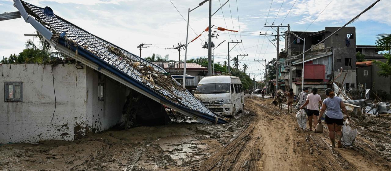 Menschen laufen durch ein Wohngebiet mit beschädigten Häusern auf den Philippinen
