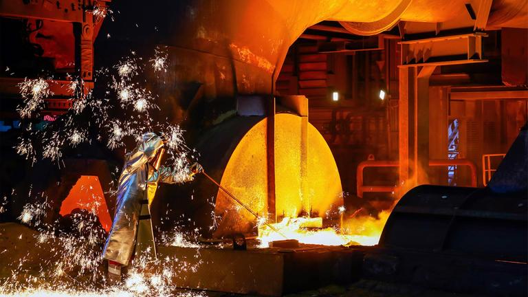 Thyssenkrupp-Stahlarbeiter im Schutzanzug entnimmt eine Roheisenprobe beim Abstich am Hochofen.